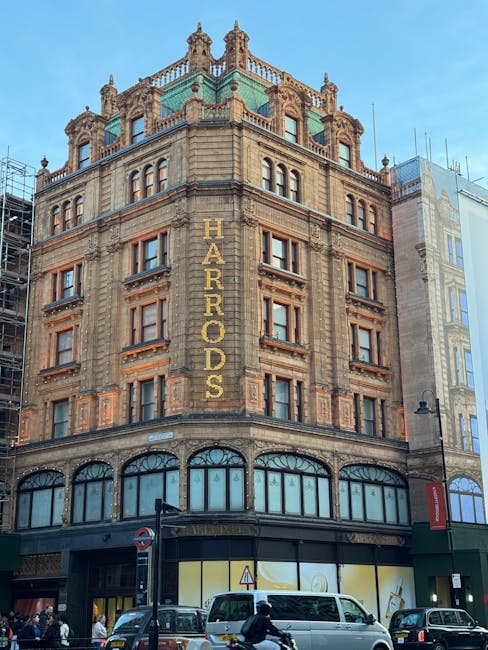 The image shows the historic Harrods department store building in Knightsbridge, London, featuring ornate architectural details and a prominent vertical sign spelling 'HARRADS' in gold lettering. The